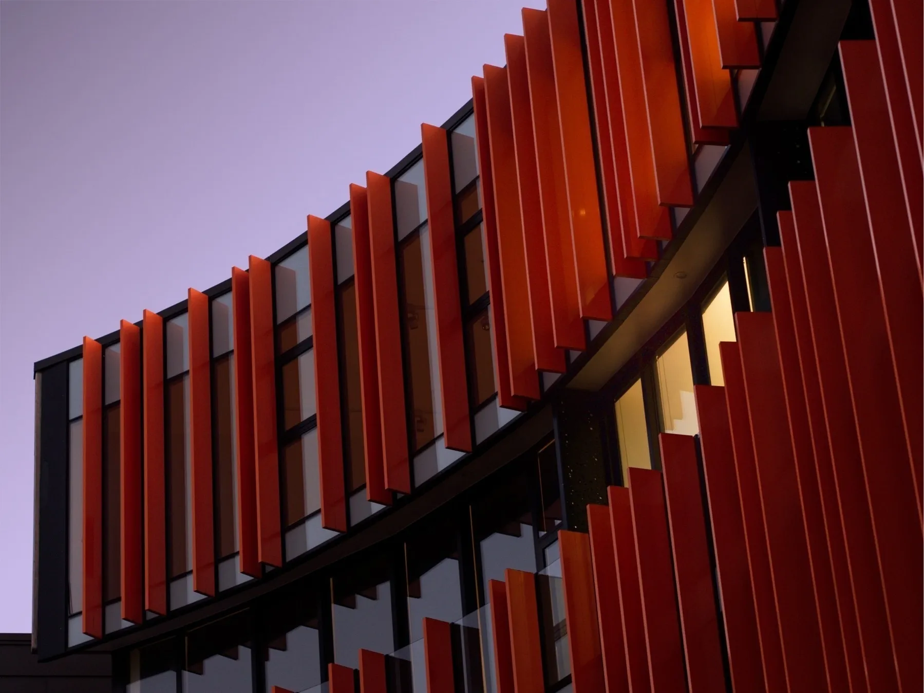A curved building with orange fins against a violet sunset sky. A yellow light focuses part of the building.