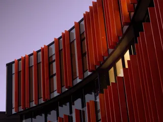 A curved building with orange fins against a violet sunset sky. A yellow light focuses part of the building.