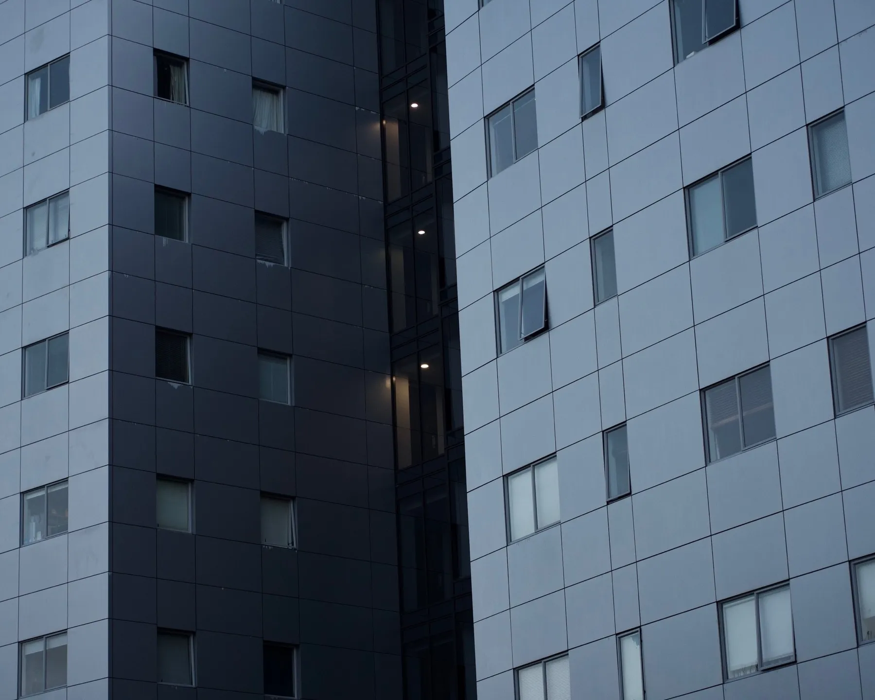 Sheer walls of a building, light blue, and a black stairwell with yellow light peeking out.